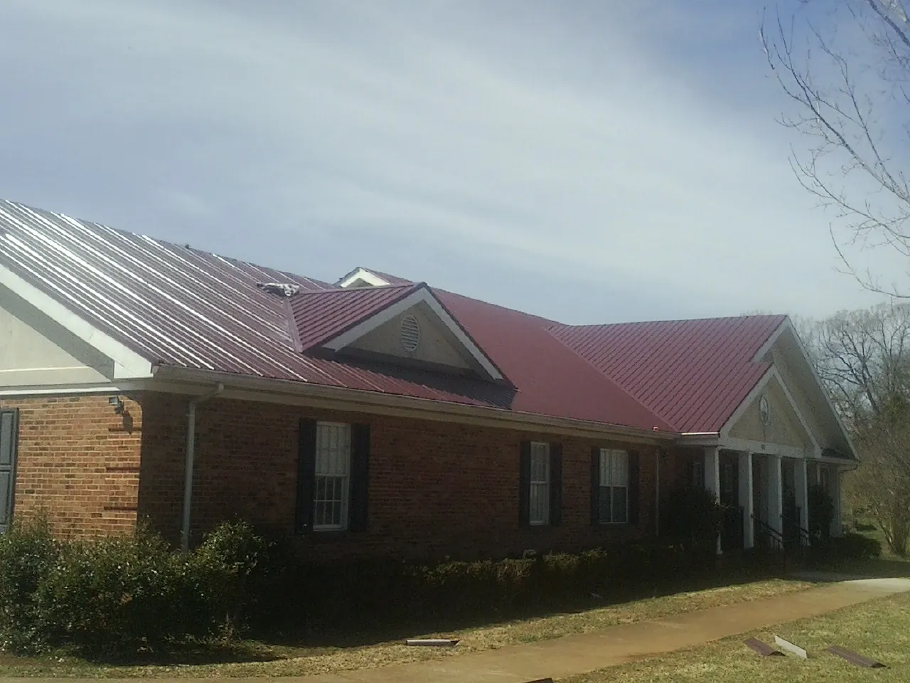 Red metal roof with gabled entries on a long brick building, from a Hail Damage Roof Repair job in Oroville